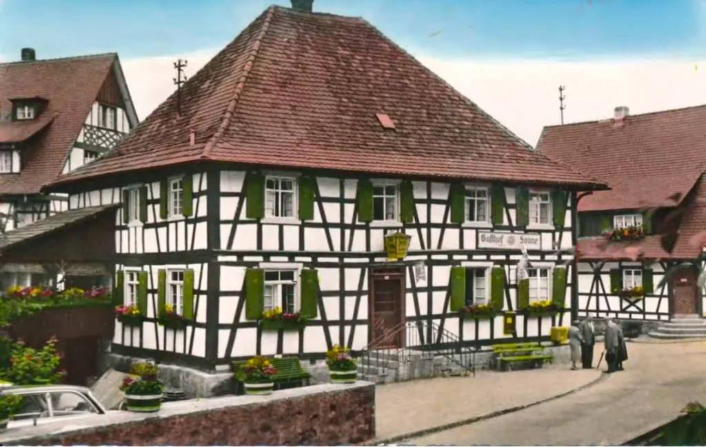 Historische Aufnahme eines Fachwerkhauses mit grünem Fensterläden und Blumenkästen im Schwarzwald, Gasthof Sonne sichtbar.