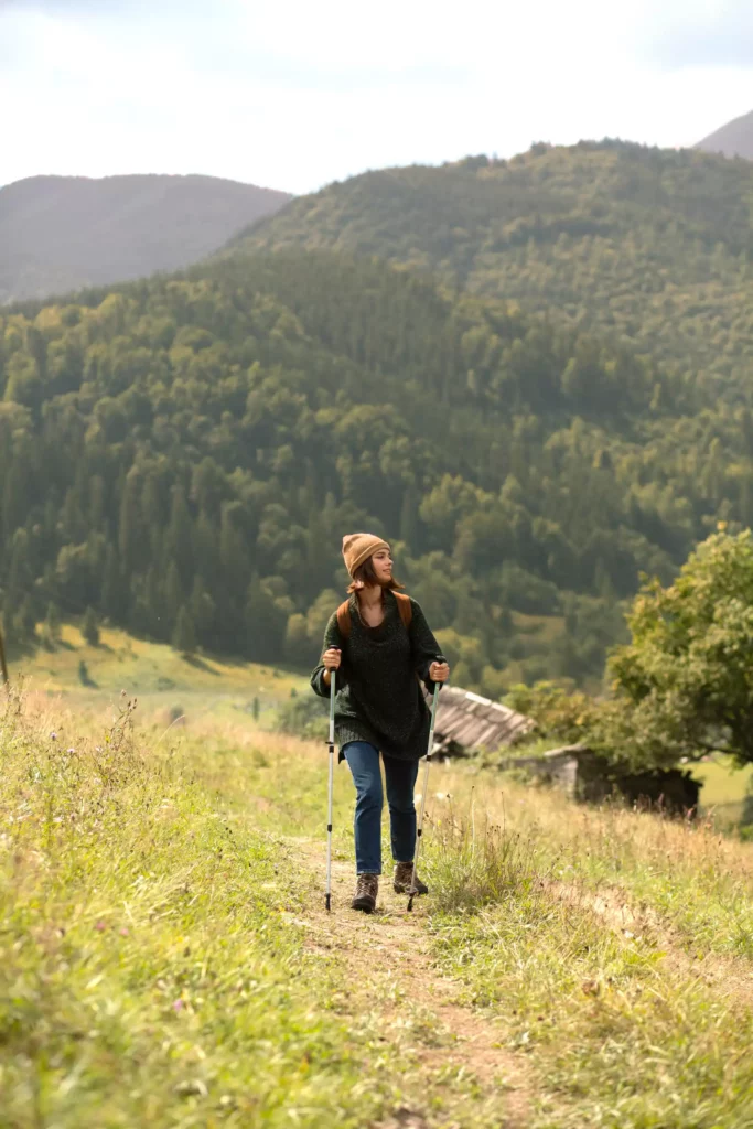 Frau mit Wanderstöcken auf einem Pfad in grüner Landschaft vor bewaldeten Schwarzwaldbergen bei Maison Talmühle Resort.