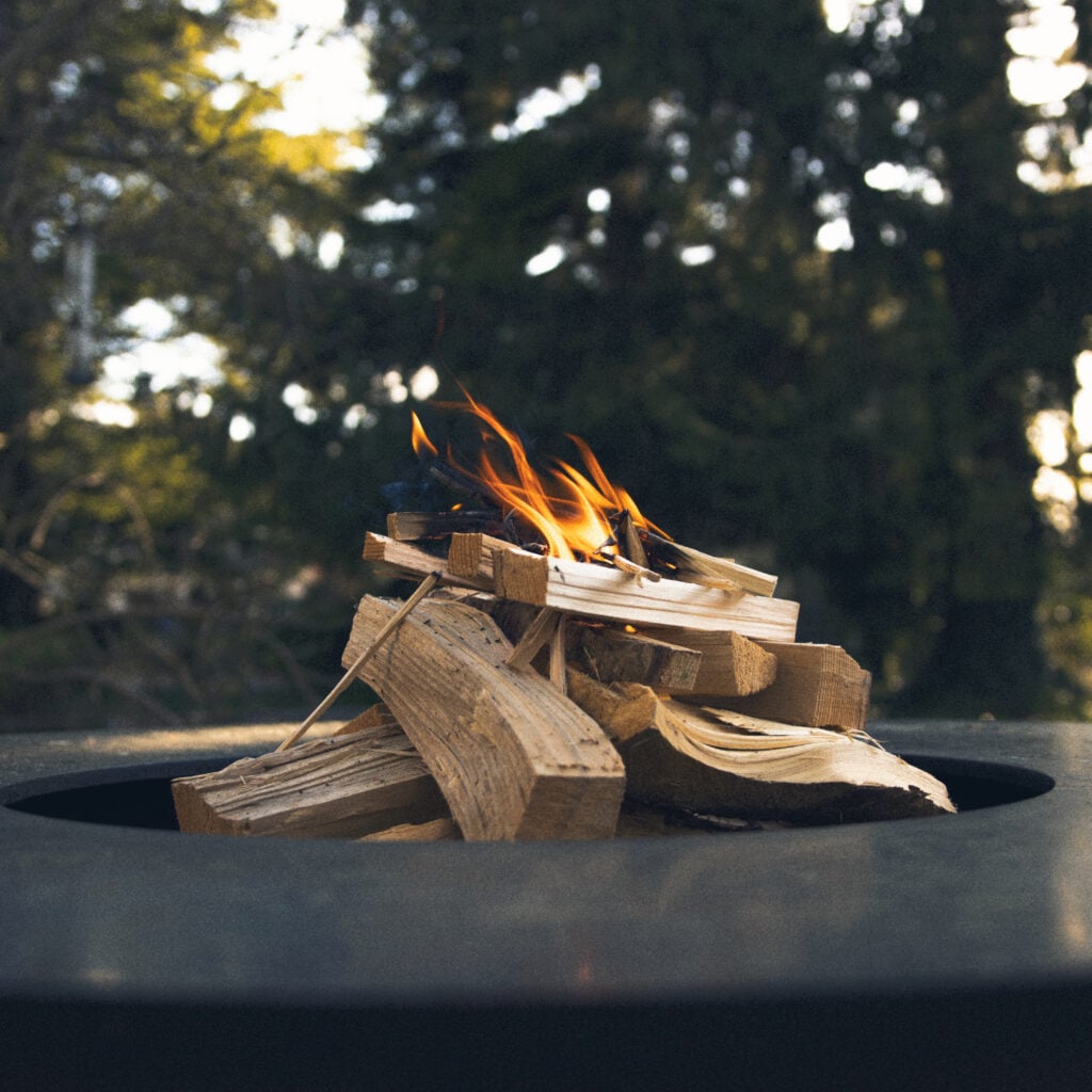 Feuerring mit brennendem Holz vor unscharfem Schwarzwald-Hintergrund im Maison Talmühle Resort Spa