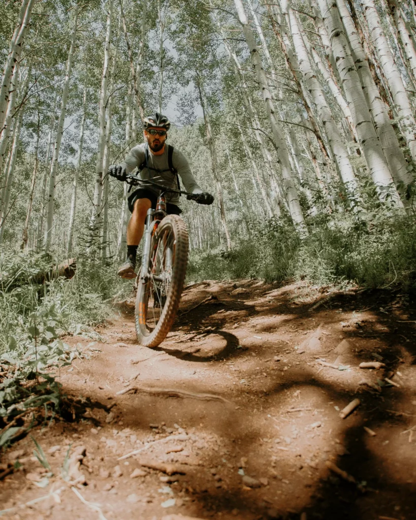 Mountainbiker mit Helm fährt auf Waldweg zwischen Birkenbäumen im Schwarzwald bei Maison Talmühle Resort Spa