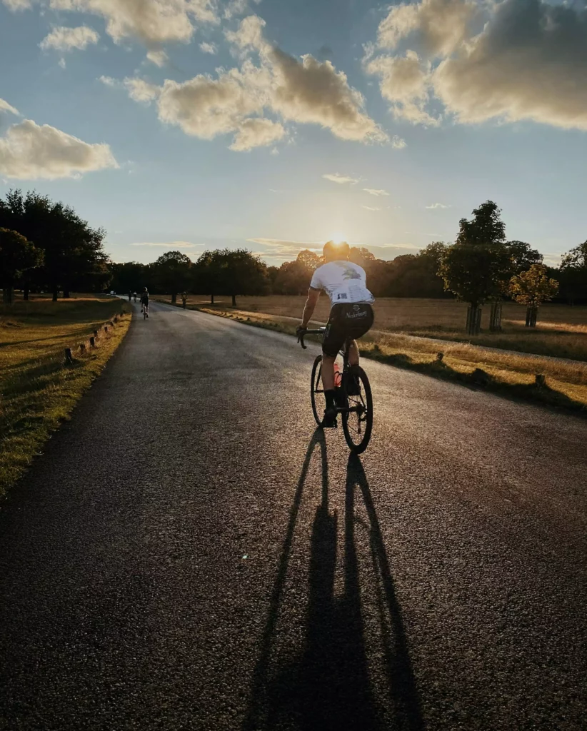 Radfahrer auf Landstraße bei Sonnenuntergang mit langen Schatten und Bäumen am Straßenrand im Schwarzwald