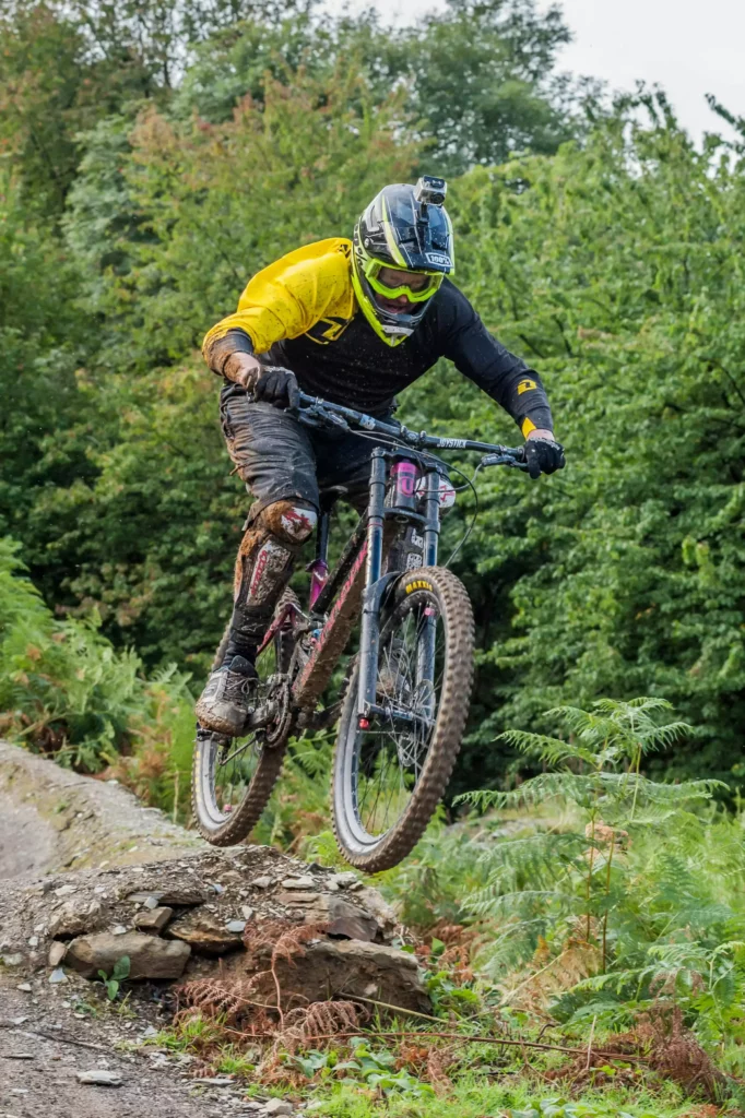 Mountainbiker mit Helm und Kamera springt auf einem Waldtrail im Schwarzwald über einen Felsen im Maison Talmühle Resort