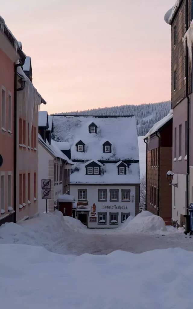 Winterliche Dorfstraße im Schwarzwald mit schneebedeckten Häusern und Eiszapfen an den Dächern bei Dämmerung