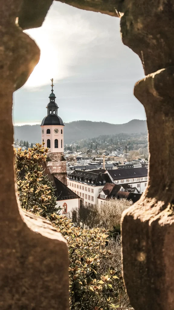 Blick durch eine steinerne Öffnung auf den Kirchturm und die Dächer von Baden-Baden im Schwarzwald bei sonnigem Wetter.