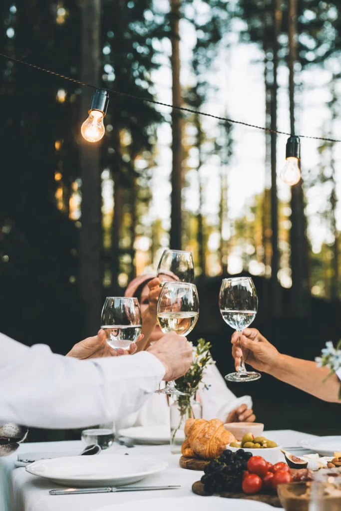 Gäste stoßen mit Weißweingläsern bei einem Abendessen im Freien im Schwarzwald Boutique Resort Maison Talmühle an