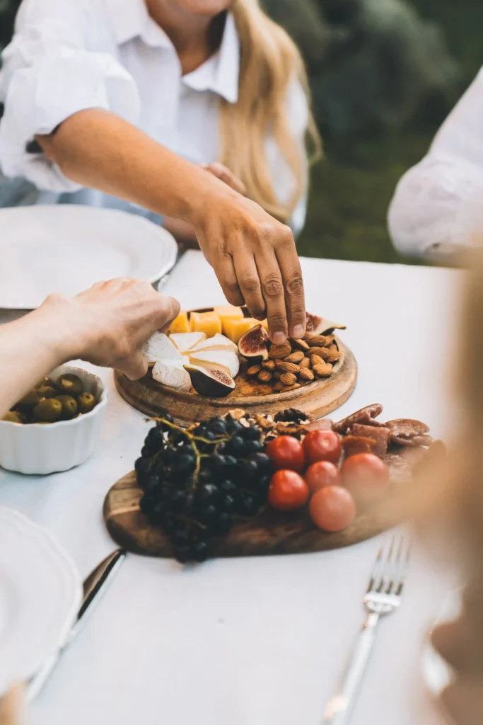 Personen greifen bei einem Dinner im Maison Talmühle Resort im Schwarzwald zu Käse, Feigen, Mandeln, Trauben und Tomaten auf