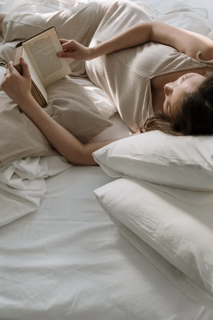 Frau liegt gemütlich auf weißem Bett mit Kissen und liest Buch in Maison Talmühle Boutique Resort Schwarzwald Spa Suite