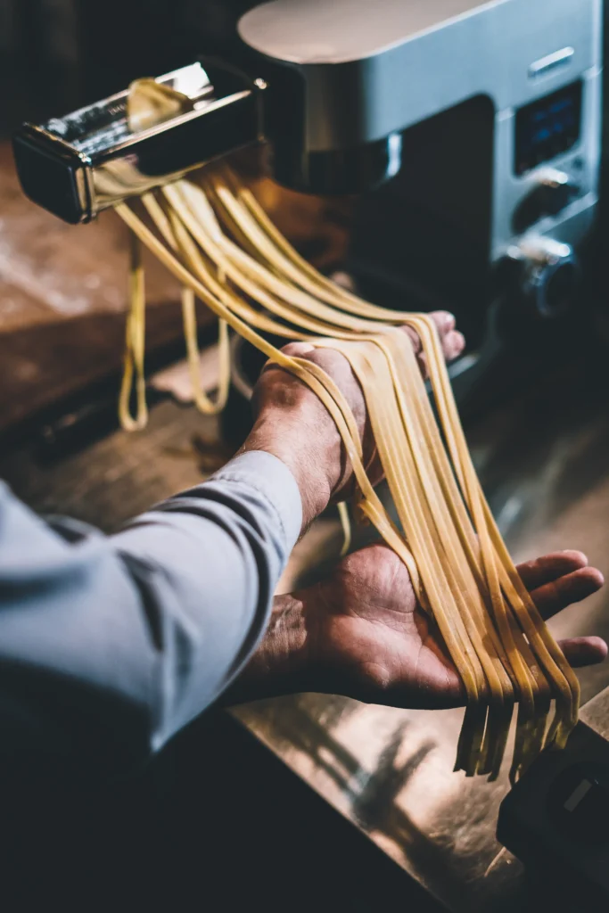 Hände halten frisch geschnittene Pasta, die aus einer Nudelmaschine in einer Küche im Schwarzwald-Resort Maison Talmühle