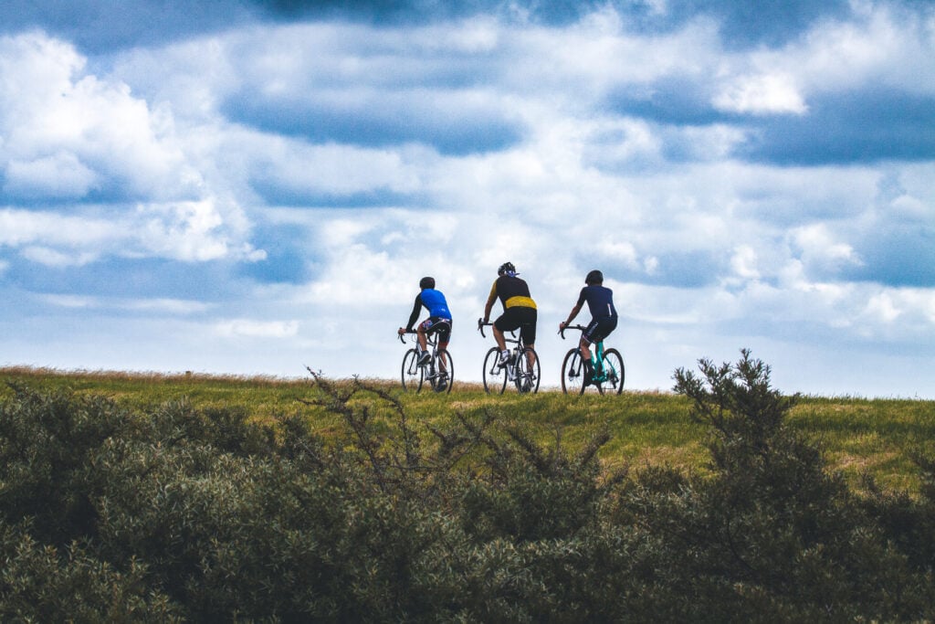 Drei Radfahrer fahren auf einem Hügel unter bewölktem Himmel in einer grünen Landschaft im Schwarzwald.
