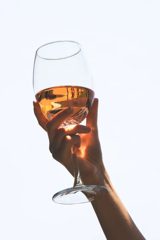 Hand hält ein Weinglas mit roséfarbenem Wein vor hellem Himmel im Schwarzwald Boutique Resort Maison Talmühle